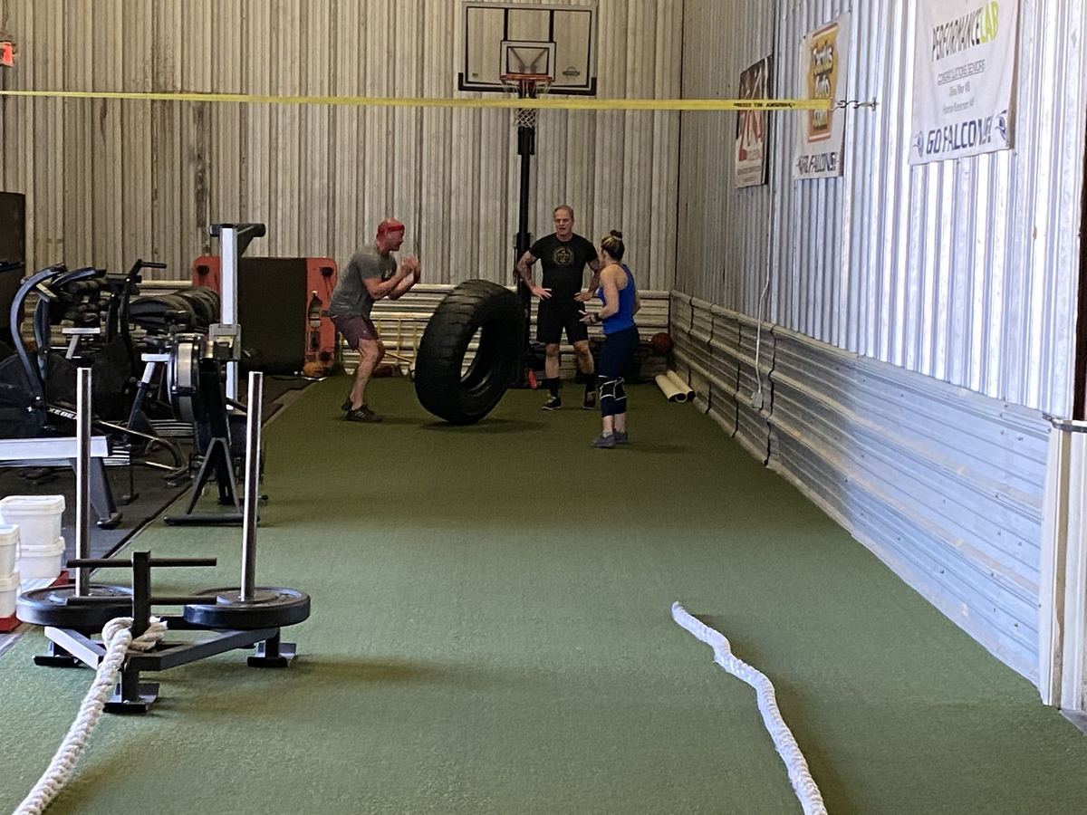 Coach John supervising clients through sled, tire, and conditioning work in the gym